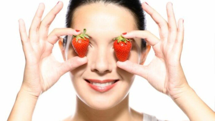A Picture of a Woman Holding Two Strawberries on Her Eyes 