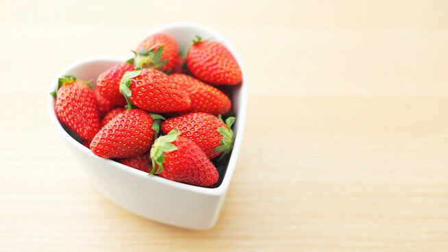 A Picture of Strawberries in heart shape bowl on wooden background