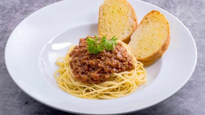Spaghetti Bolognese with Two Slices of Garlic Bread in a White Plate