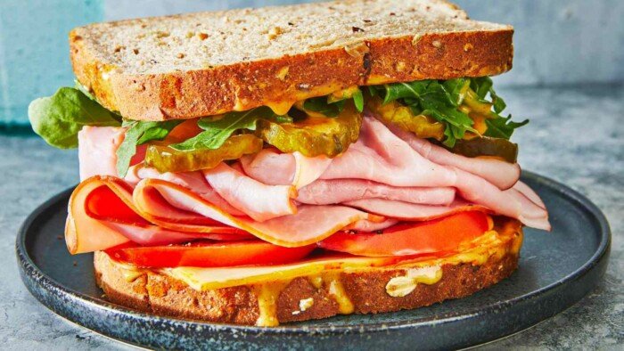 A Ham Sandwich with Cheese, Tomatoes ,Pickles made out of Brown Bread 